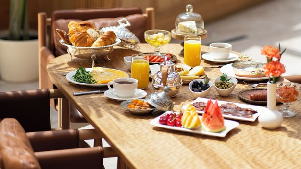 Une table de petit-déjeuner avec divers aliments, une tasse de café et un verre de jus d’orange.