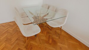 Un comedor con una mesa de vidrio rodeada por seis sillas blancas con patas doradas.