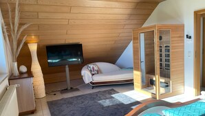 A modern bedroom with a sloped ceiling, a bed with patterned bedding, a television on a stand, and a wooden wardrobe. - 152 m² vacation apartment Quiet location on the edge of the village Overlooking the Rhine Valley Opposite the Loreley (Sankt Goar)