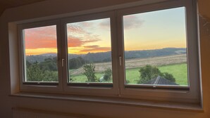 A window with a view of a sunset over a rural landscape. - 152 m² vacation apartment Quiet location on the edge of the village Overlooking the Rhine Valley Opposite the Loreley (Sankt Goar)