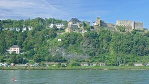 A castle on a hill with a river in the foreground. - 152 m² vacation apartment Quiet location on the edge of the village Overlooking the Rhine Valley Opposite the Loreley (Sankt Goar)
