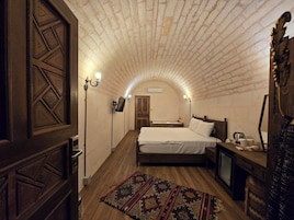 Un dormitorio con techo de ladrillo, una cama, una mesita de noche, una lámpara y una alfombra estampada.