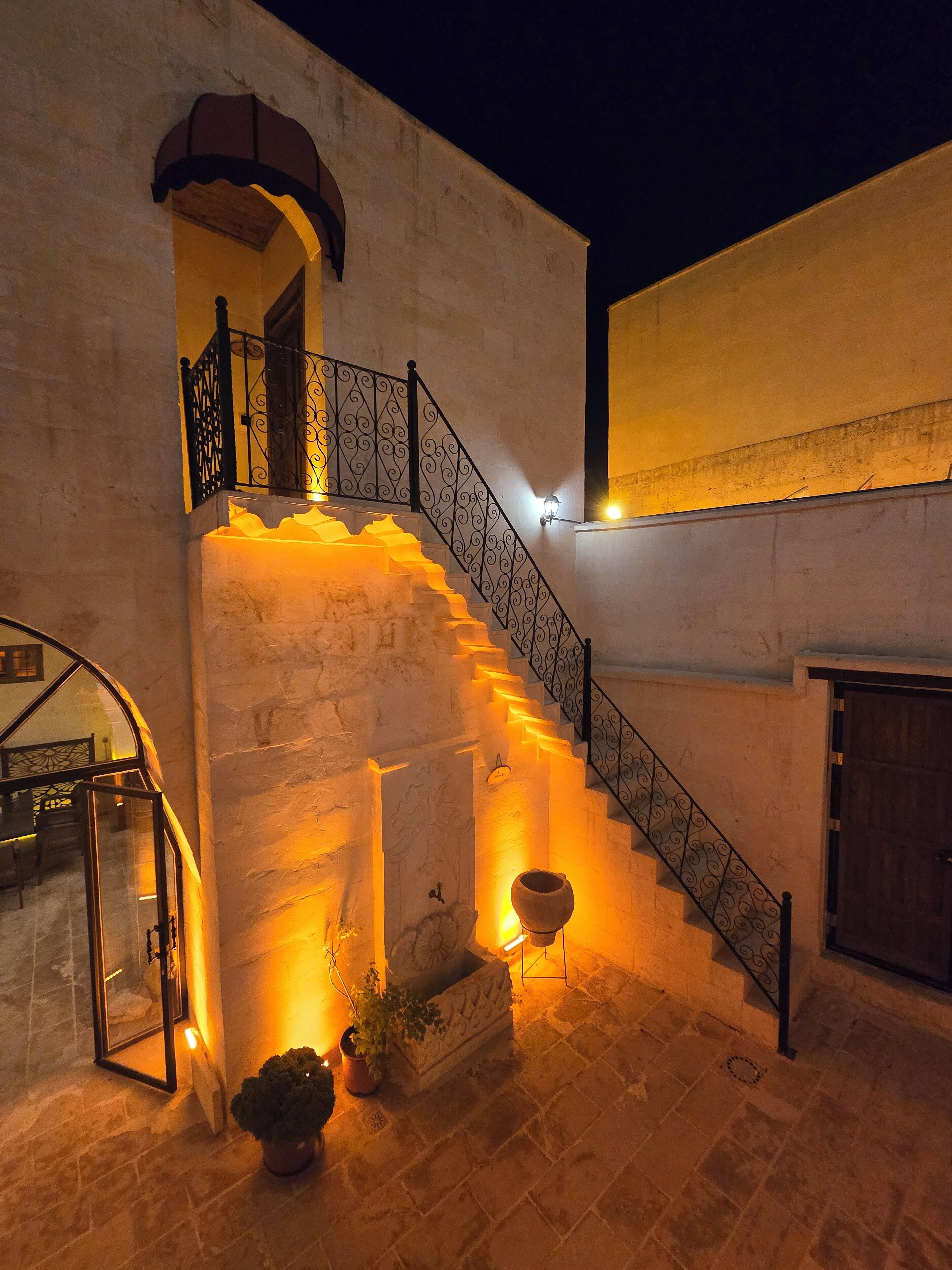 Una escalera de piedra con barandillas de metal decoradas que lleva a un balcón en el segundo piso.