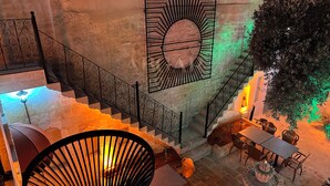 Una scala con ringhiere in metallo decorate, un muro in pietra e una sala da pranzo con tavoli e sedie.