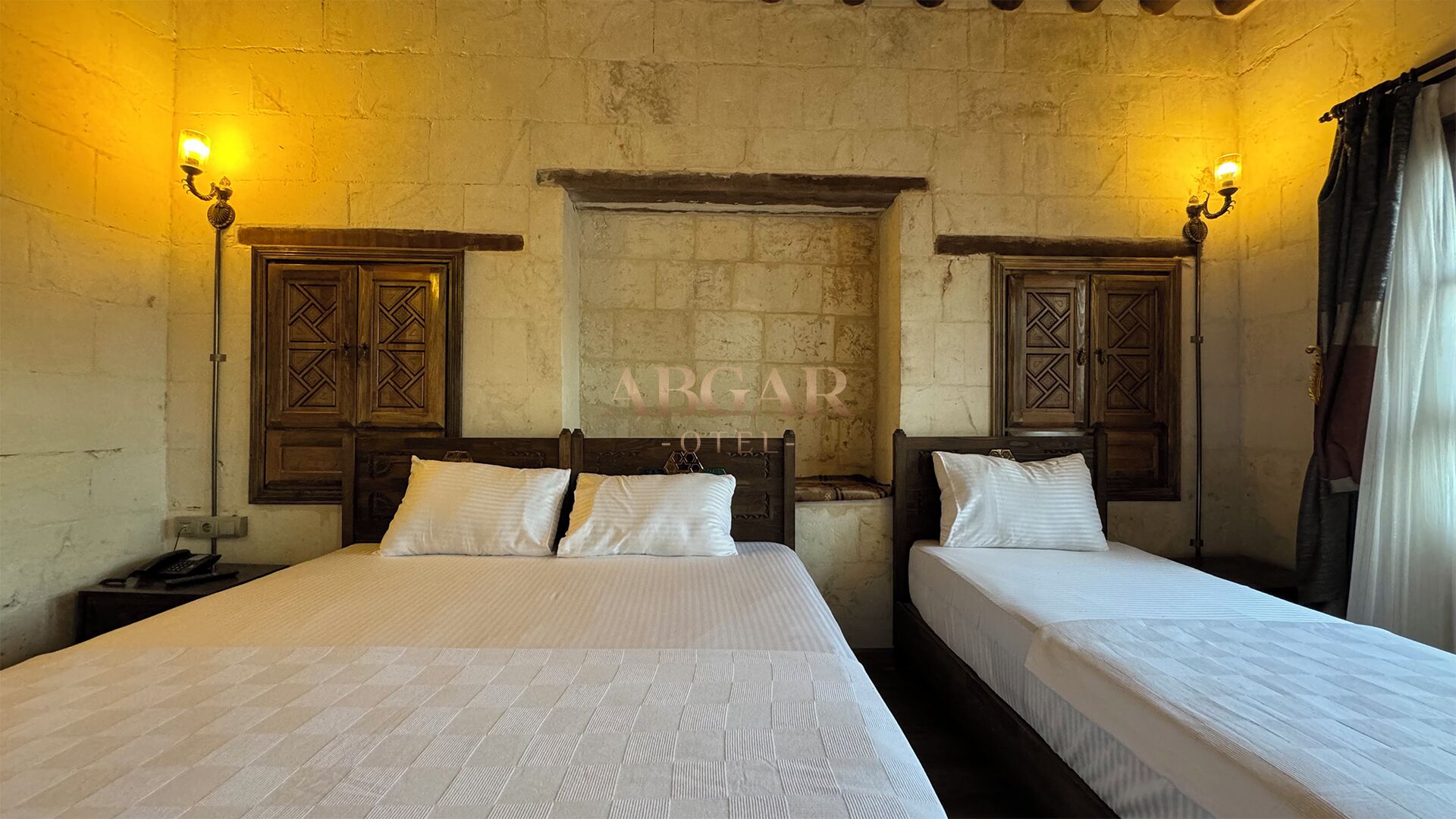 A room with two beds, wooden headboards, and a stone wall with the text "ARGAR HOTEL" in the center.