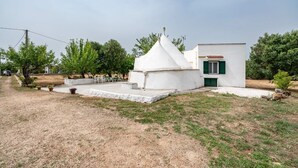 A small white building with a conical roof, a door with green shutters, and a small porch area. - Il Trullo di Nonna Ratuccia by Rentbeat (Ostuni)