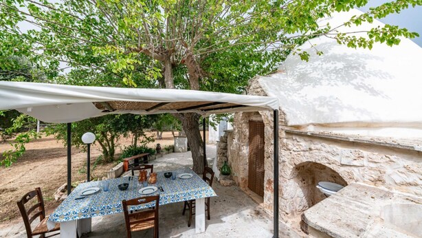An outdoor dining area with a table set for two, surrounded by stone walls and a tree. - Il Trullo di Nonna Ratuccia by Rentbeat (Ostuni)