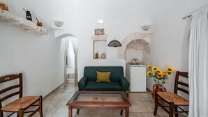 A living room with a green sofa, wooden chairs, a coffee table, a white fireplace, and a small white cabinet. - Il Trullo di Nonna Ratuccia by Rentbeat (Ostuni)