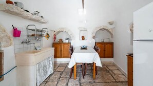 A kitchen with a stone floor, wooden cabinets, a white table, and a hanging pot rack. - Il Trullo di Nonna Ratuccia by Rentbeat (Ostuni)