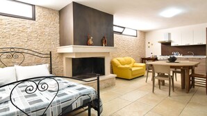 A bedroom with a bed, a fireplace, a yellow armchair, a dining table, and a kitchen area. - Casa Carlà by Rentbeat (Surbo)