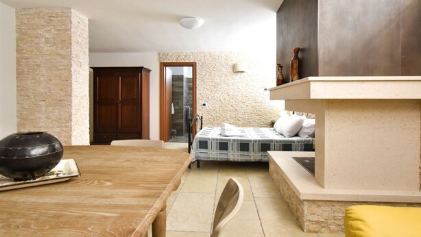 A room with a wooden dining table, a bed with a striped bedspread, a stone wall, and a wooden door. - Casa Carlà by Rentbeat (Surbo)