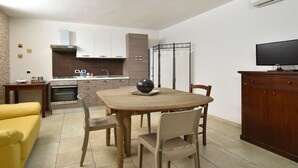 A dining area with a table, chairs, a sofa, a kitchen with cabinets, a stove, and an air conditioning unit. - Casa Carlà by Rentbeat (Surbo)