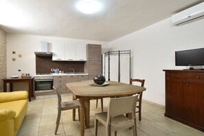 A dining area with a table, chairs, a sofa, a kitchen with cabinets, a stove, and an air conditioning unit. - Casa Carlà by Rentbeat (Surbo)