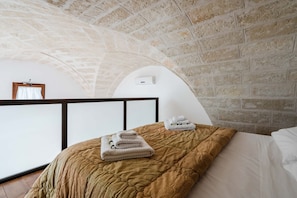 A bedroom with a brick ceiling, a bed with a brown quilt, and a white bedside table with towels.