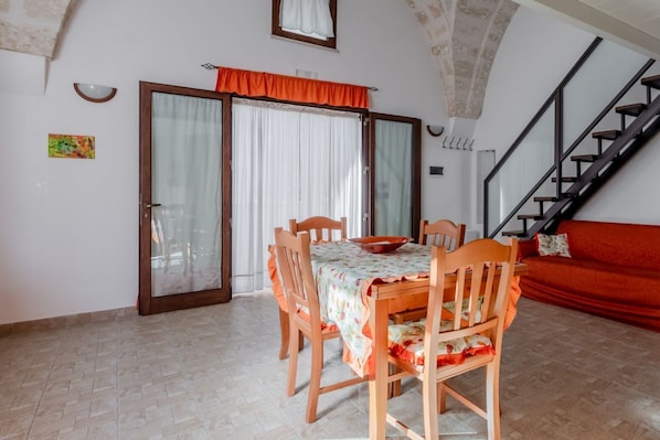 A dining area with a table and chairs, a red sofa, a staircase, and a door with curtains.