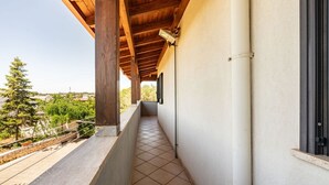 A covered balcony with a tiled floor, wooden beams, a wall-mounted light, and a window with a black frame. - Apart Irene by Rentbeat (Ostuni)