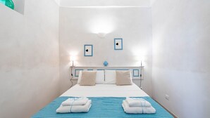 A small, single-bed room with a striped bedspread, two pillows, and a bedside table with a lamp. - Il Vico 113 Ostuni by Rentbeat (Casoria)