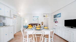 A dining area with a white table, four chairs, and a television on a white cabinet. - Il Vico 113 Ostuni by Rentbeat (Casoria)