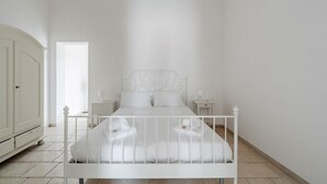Een wit hemelbed met hoofdbord, twee nachtkastjes en een kledingkast.
