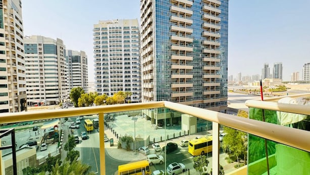 A high-rise building with multiple floors and balconies, a parking area with cars and a yellow bus, and a clear sky. - OYO 1233 Home Elite 1 Residence Sports City, Dubai (Dubai)
