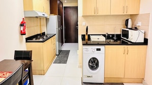 A compact kitchen with wooden cabinets, a washing machine, a microwave, and a gas stove. - OYO 1233 Home Elite 1 Residence Sports City, Dubai (Dubai)