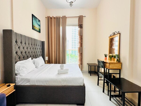 A bedroom with a large bed, a desk, a chair, a mirror, and a window with curtains.