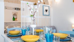 A dining area with a table set with yellow and blue plates, glasses, and a vase with flowers. - Il Vico 8 Ostuni by Rentbeat (Ostuni)