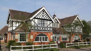 A traditional Tudor-style building with a symmetrical facade, large windows, and a white picket fence. - St George's Lodge (Woking)