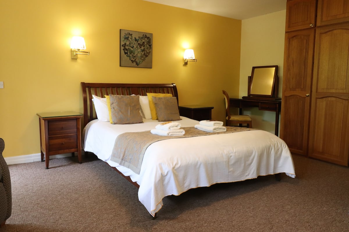 Una cama bien hecha con almohadas y una manta, una mesita de noche con lámpara, un armario de madera y un cuadro enmarcado en la pared.