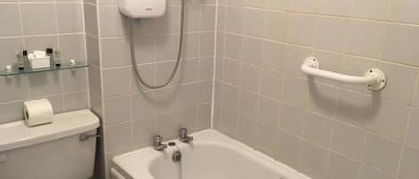 A bathroom with a toilet, a glass shelf with toiletries, a shower with a handheld showerhead, and a bathtub with a grab bar.