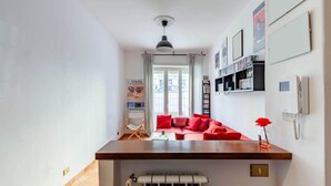 A compact living space with a kitchenette, a red sofa, a small table, and a radiator. - Casa Giancarlo by Rentbeat (Roma)