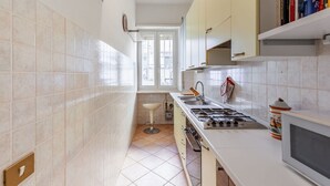 A kitchen with white cabinets, a gas stove, a microwave, and a window. - Casa Giancarlo by Rentbeat (Roma)