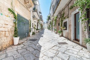 A narrow stone-paved street flanked by buildings with balconies, potted plants, and a clear sky. - Il Vico Suite Ostuni by Rentbeat (Ostuni)