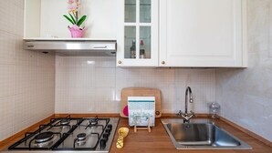 A kitchen with a gas stove, stainless steel sink, white cabinets, and a wooden cutting board. - Casa Cenzina by Rentbeat (Locorotondo)
