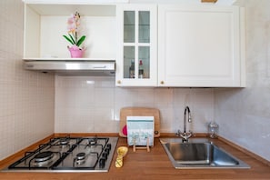 A kitchen with a gas stove, stainless steel sink, white cabinets, and a wooden cutting board. - Casa Cenzina by Rentbeat (Locorotondo)