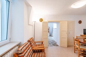 A room with a window, a radiator, a bench, a table with chairs, and a door leading to another room. - Casa Cenzina by Rentbeat (Locorotondo)