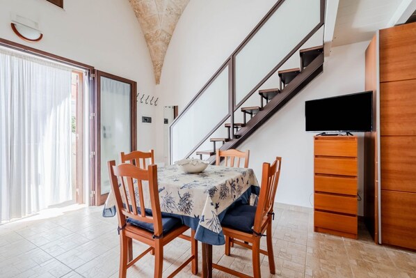 A dining area with a table, chairs, a television, and a staircase.