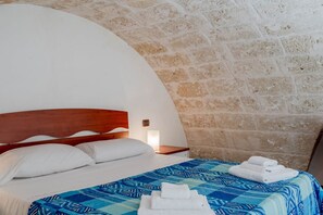 A bedroom with a wooden headboard, a patterned bedspread, and a stone wall.
