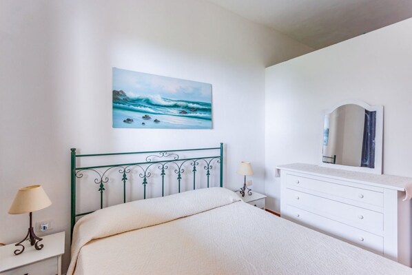 Ein Schlafzimmer mit Bett, Nachttisch, Schminktisch und Spiegel, sowie einem Bild einer Strandlandschaft.