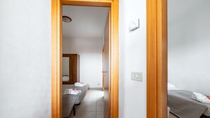 Et hotelværelse med en trædørkarm, en seng med gråt sengetæppe, et natbord og en vægmonteret lampe.