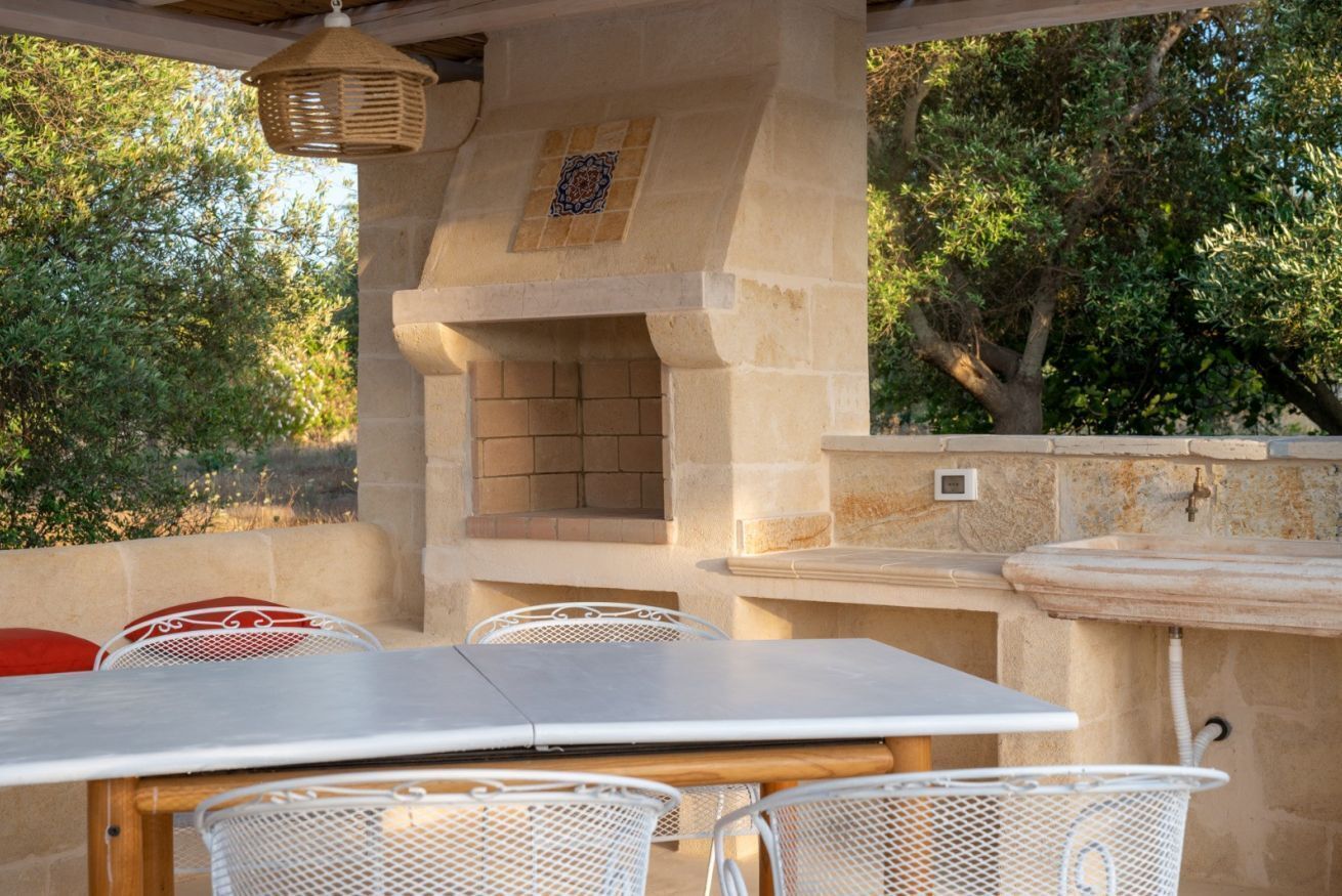 Eine Terrasse im Freien mit einem Steinofen, weißen Metallstühlen und einem Tisch.