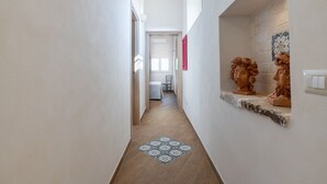 A narrow hallway with a patterned floor, a door leading to a room, and a wall-mounted shelf with sculptures.