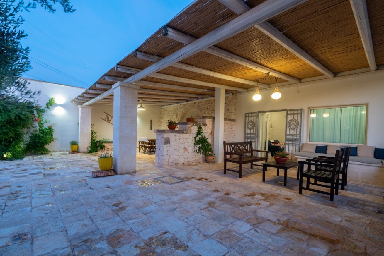 An outdoor patio area with stone flooring, wooden beams, a stone wall, and seating furniture.