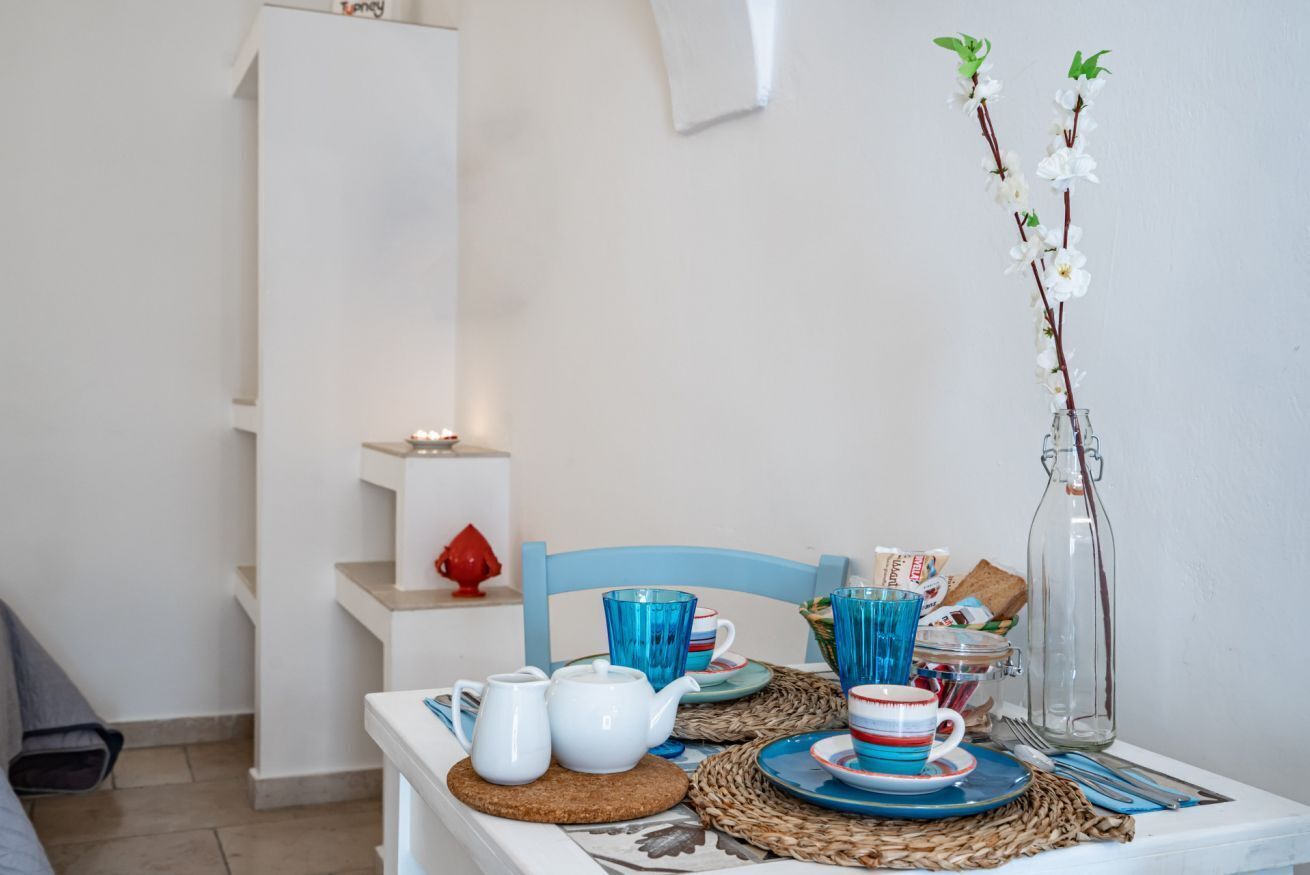 Una mesa de comedor con vajilla azul y blanca, una botella de vidrio transparente y un florero con flores blancas.