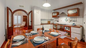 Et spiseområde med et træbord dækket til fire personer, et køkken med hvide skabe og et flisebeklædt backsplash samt en spejlvæg.