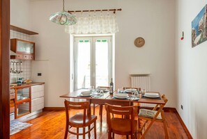 Uma sala de jantar com mesa e cadeiras de madeira, cozinha com armários brancos e uma janela com vista.