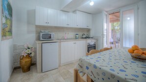 A compact kitchen with white cabinets, a microwave, a small refrigerator, and a dining table with a patterned tablecloth. - Il Lilla by Rentbeat (Locorotondo)