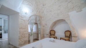A bedroom with stone walls, a bed with rolled towels, two chairs, and a window with a curtain. - Il Lilla by Rentbeat (Locorotondo)