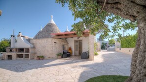 A stone courtyard with a pergola, potted plants, and a tree. - Il Lilla by Rentbeat (Locorotondo)