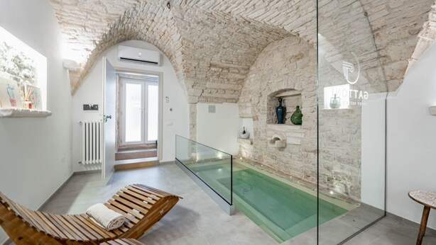 Une salle de spa dotée d’un jacuzzi en verre, de chaises longues en bois et d’un mur en pierre.